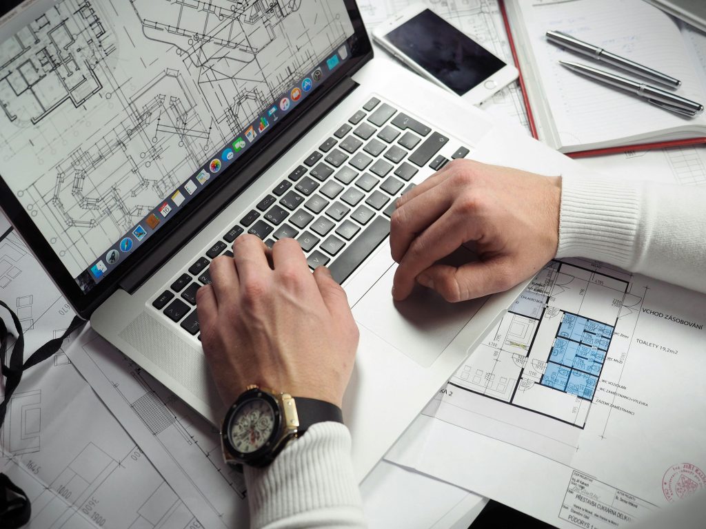 Architect reviewing detailed floor plans and schematics on a laptop with a smartphone nearby.