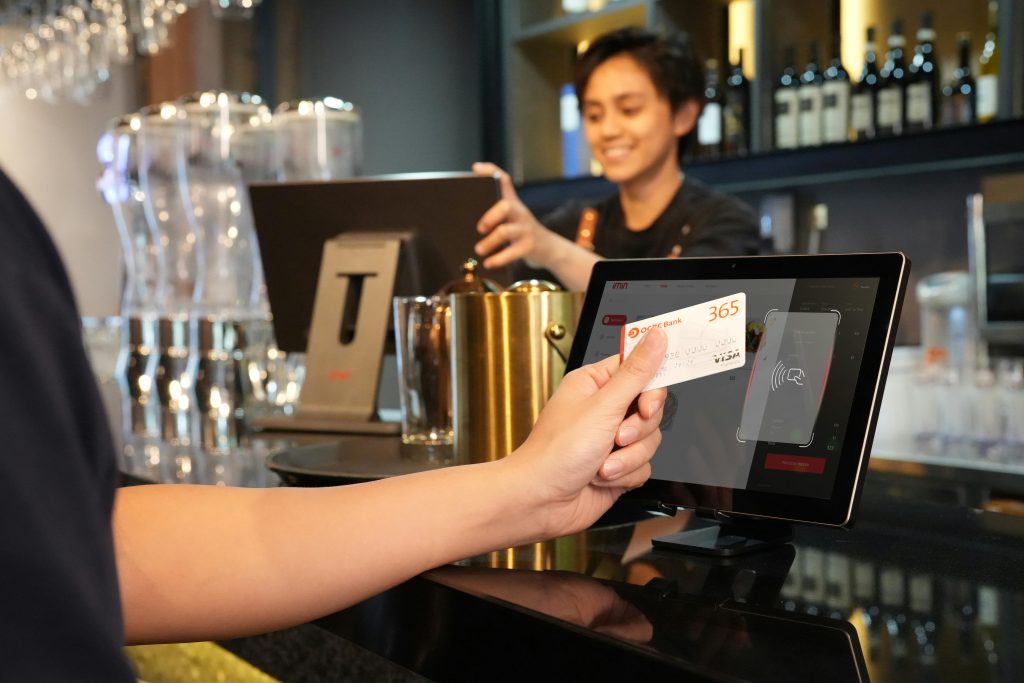 Person using contactless credit card payment at a modern bar, assisted by a cashier.