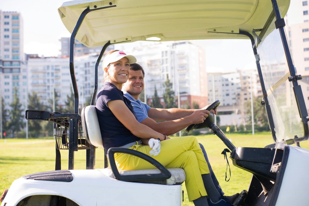 Smiling couple enjoying a golf cart ride in a sunny urban park, Portugal.